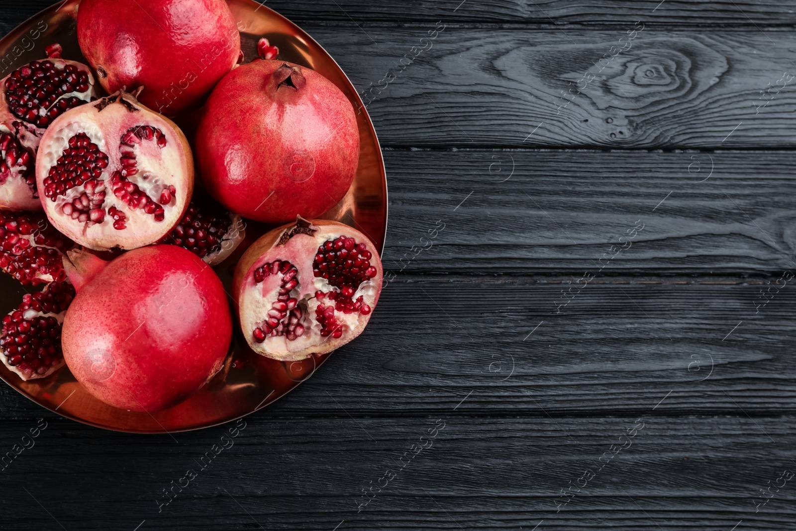 Photo of Delicious ripe pomegranates on black wooden table, top view. Space for text