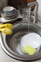 Photo of Washing plates, sponge and rubber gloves in kitchen sink