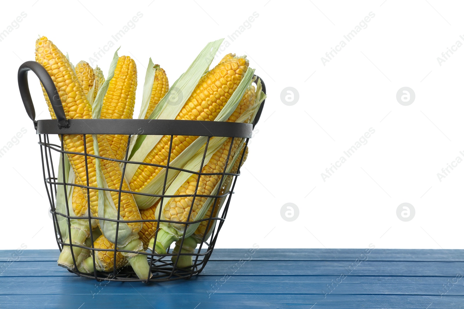 Photo of Tasty fresh corn cobs in basket on blue wooden table against white background