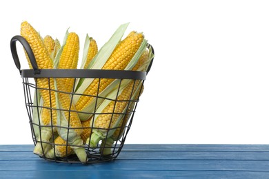 Photo of Tasty fresh corn cobs in basket on blue wooden table against white background