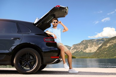 Happy man sitting in trunk of modern car in mountains