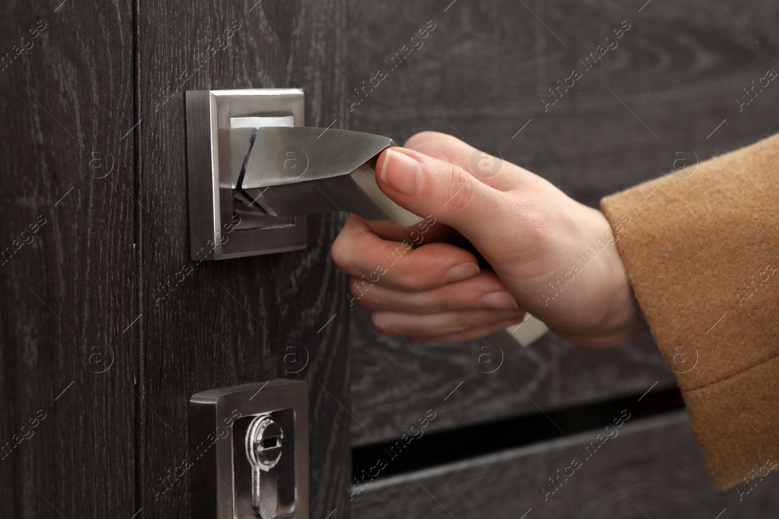 Photo of Woman opening wooden door indoors, closeup of hand on handle