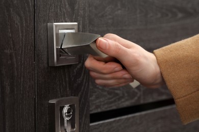 Woman opening wooden door indoors, closeup of hand on handle