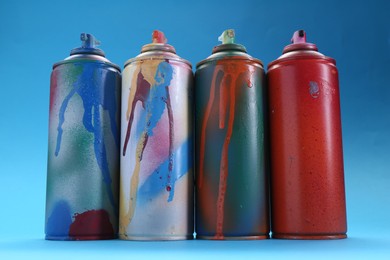 Photo of Many spray paint cans on light blue background, low angle view