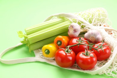 Photo of String bag with different vegetables on light green background, closeup