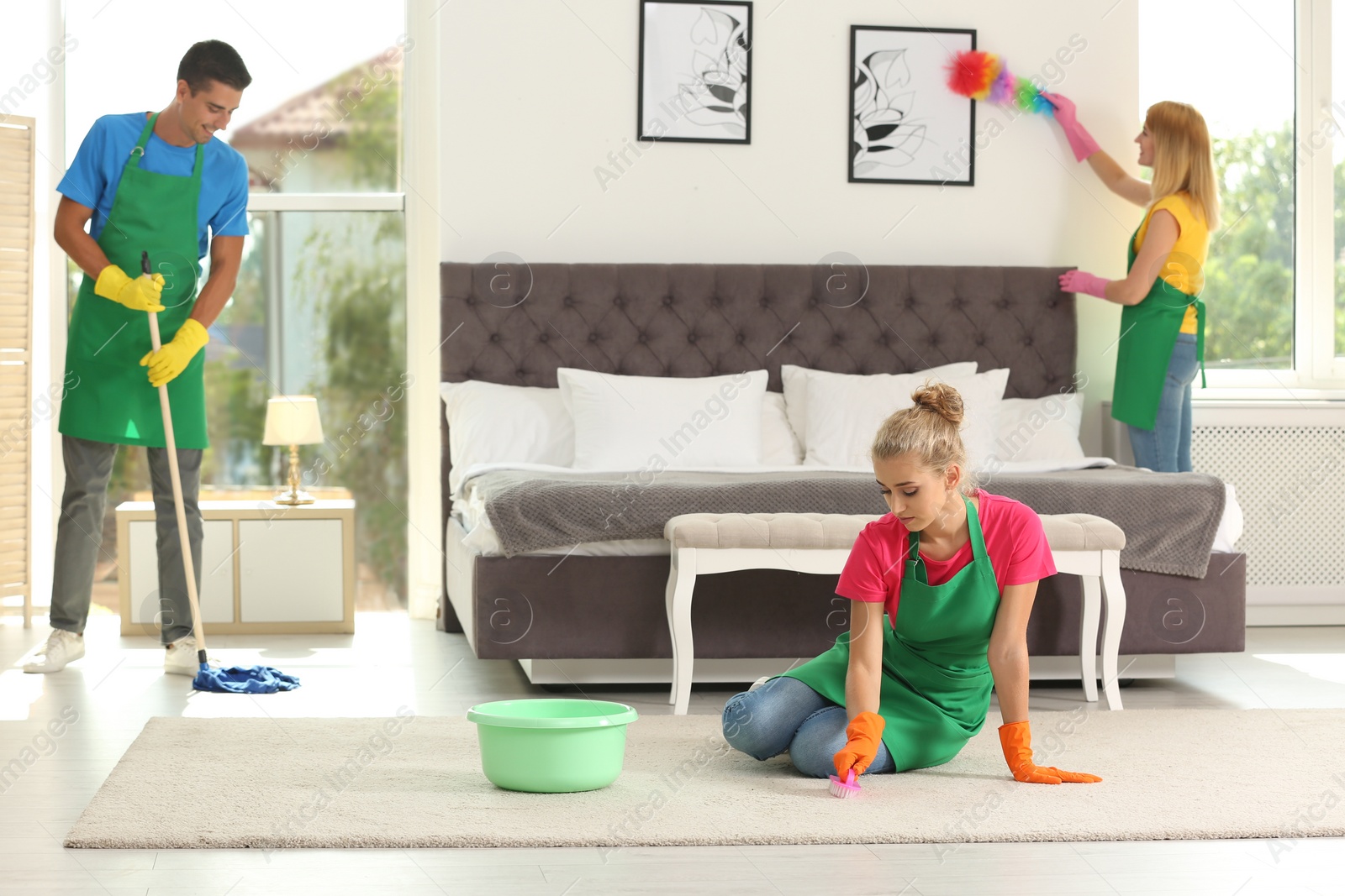 Photo of Team of professional janitors in uniform cleaning bedroom