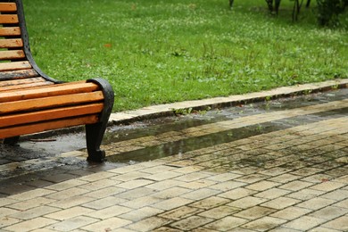 Puddle of rain water near wooden bench on paved pathway in park