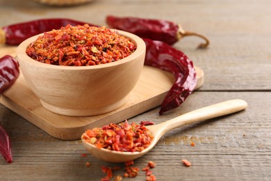 Aromatic spice. Red chili pepper flakes in bowl, spoon and pods on wooden table, closeup