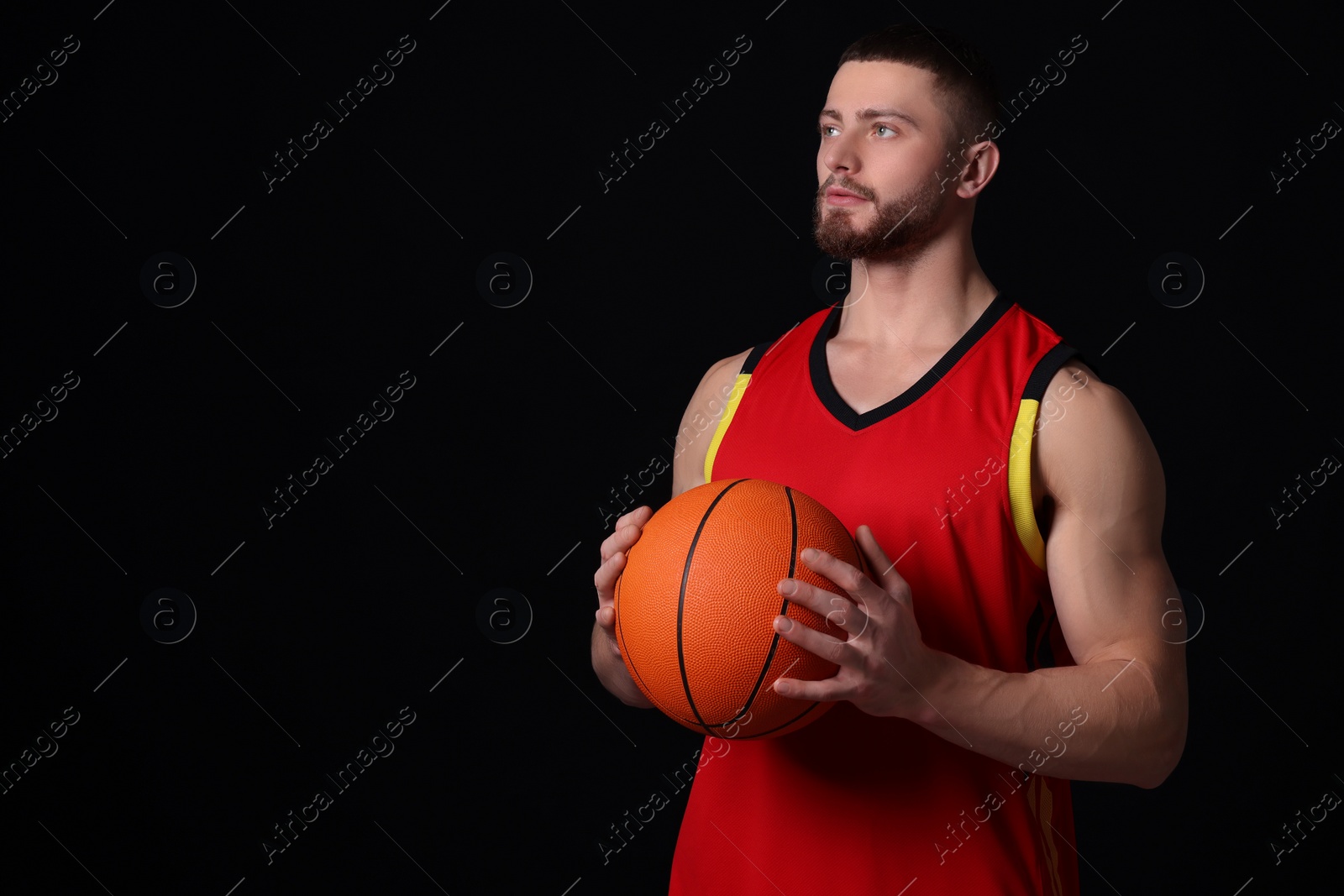 Photo of Athletic young man with basketball ball on black background. Space for text