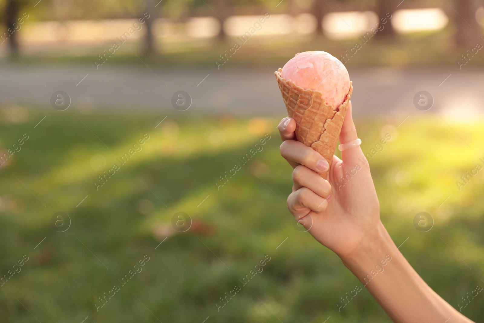 Photo of Woman holding delicious ice cream in waffle cone outdoors, closeup of hand. Space for text