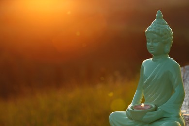 Photo of Decorative Buddha statue with burning candle on log outdoors at sunset. Space for text