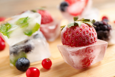 Photo of Ice cubes with different berries and mint on wooden board, closeup
