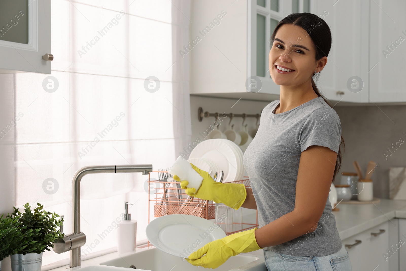 Photo of Happy woman washing plate at sink in kitchen