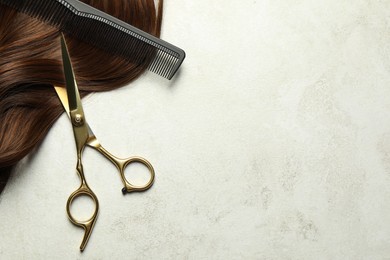 Photo of Professional hairdresser scissors and comb with brown hair strand on grey table, top view. Space for text