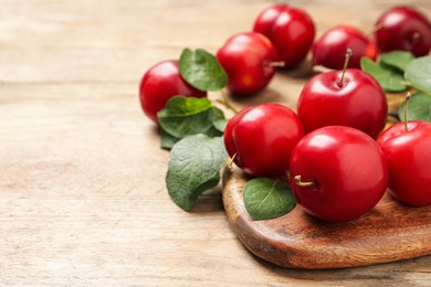 Photo of Delicious ripe cherry plums with leaves on wooden table, closeup. Space for text