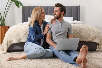 Photo of Happy couple with laptop on floor in bedroom