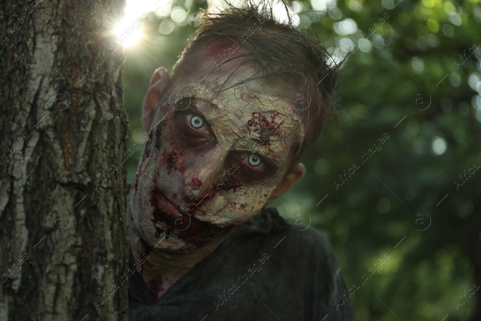 Photo of Scary zombie near tree outdoors. Halloween monster