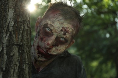 Scary zombie near tree outdoors. Halloween monster