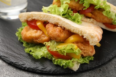 Photo of Delicious pita sandwiches with fried fish, pepper, tomatoes and lettuce on dark grey table, closeup