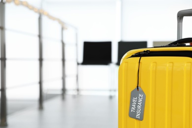 Yellow suitcase with label indoors, space for text. Travel insurance