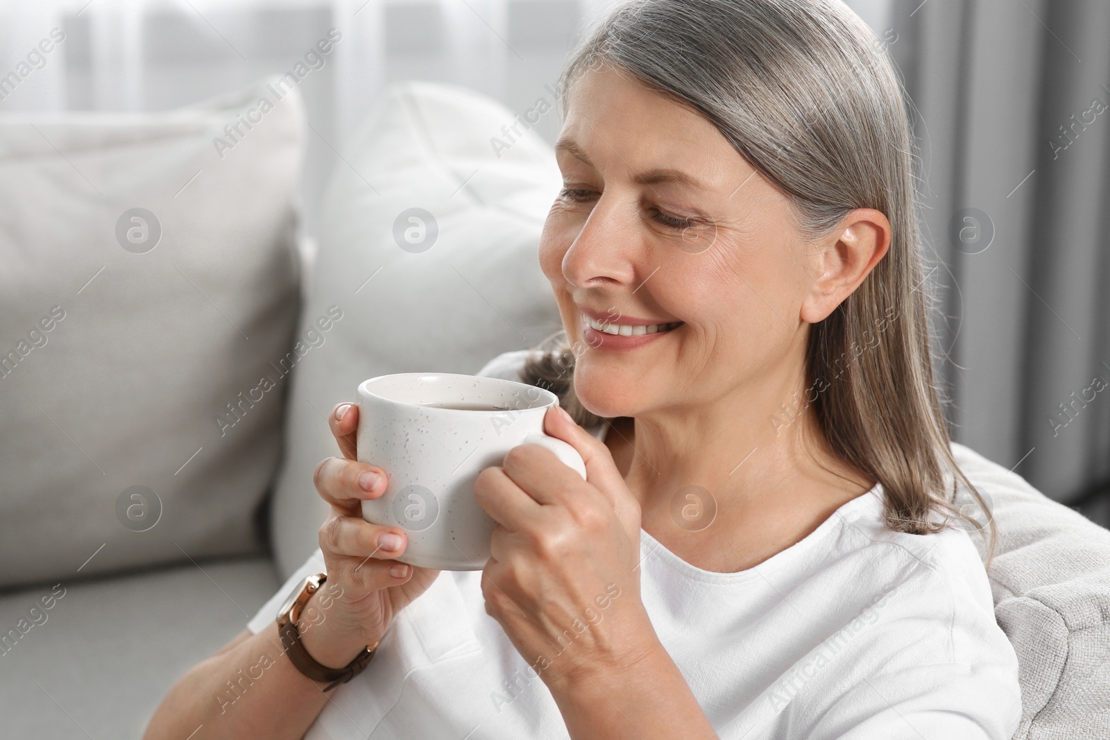 Photo of Senior woman with cup of tea on sofa at home