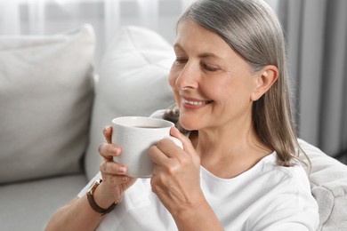 Photo of Senior woman with cup of tea on sofa at home