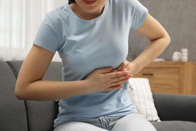 Woman suffering from stomach pain on sofa indoors, closeup