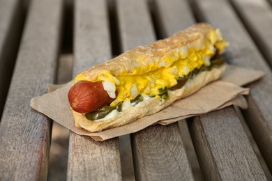 Photo of Fresh tasty hot dog with sauce on wooden surface outdoors, closeup
