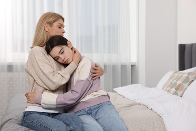 Photo of Mother consoling her upset daughter in bedroom, space for text. Teenager problems