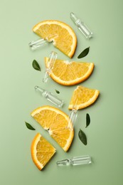 Skincare ampoules with vitamin C, slices of orange and leaves on light green background, flat lay