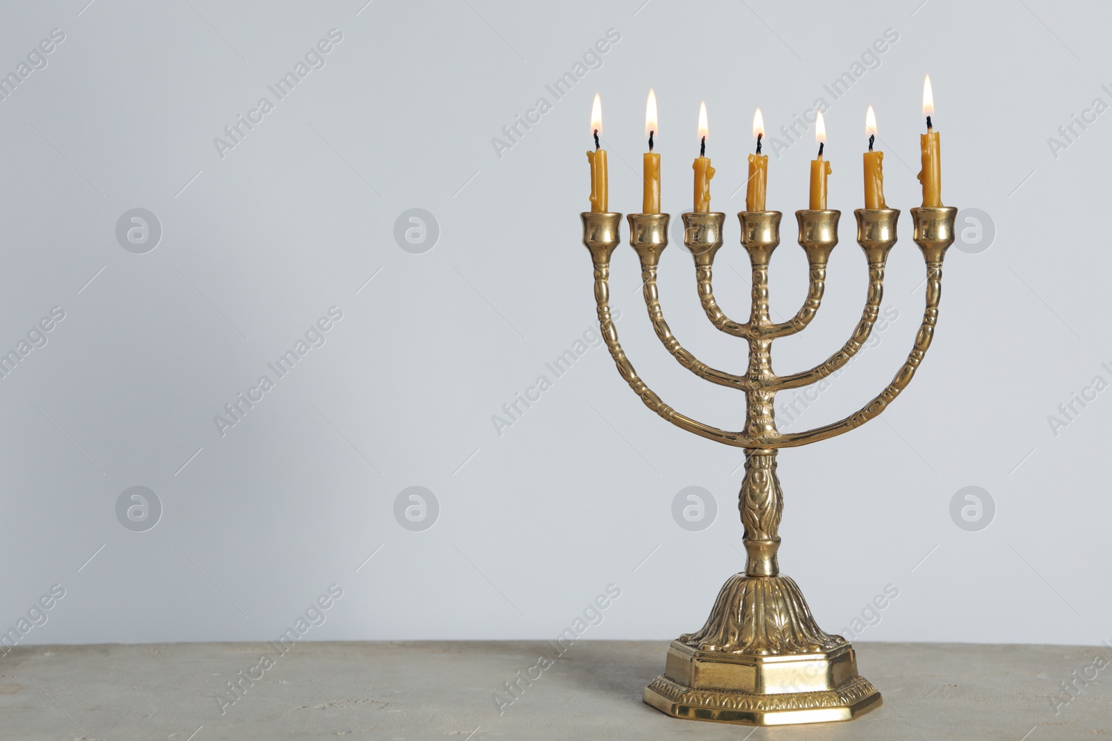 Photo of Golden menorah with burning candles on table against light grey background, space for text