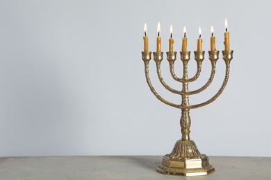 Photo of Golden menorah with burning candles on table against light grey background, space for text