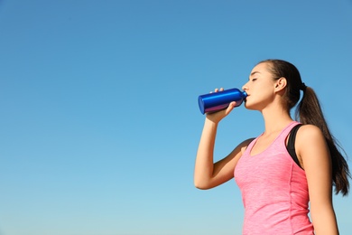 Young sporty woman drinking from water bottle outdoors on sunny day. Space for text