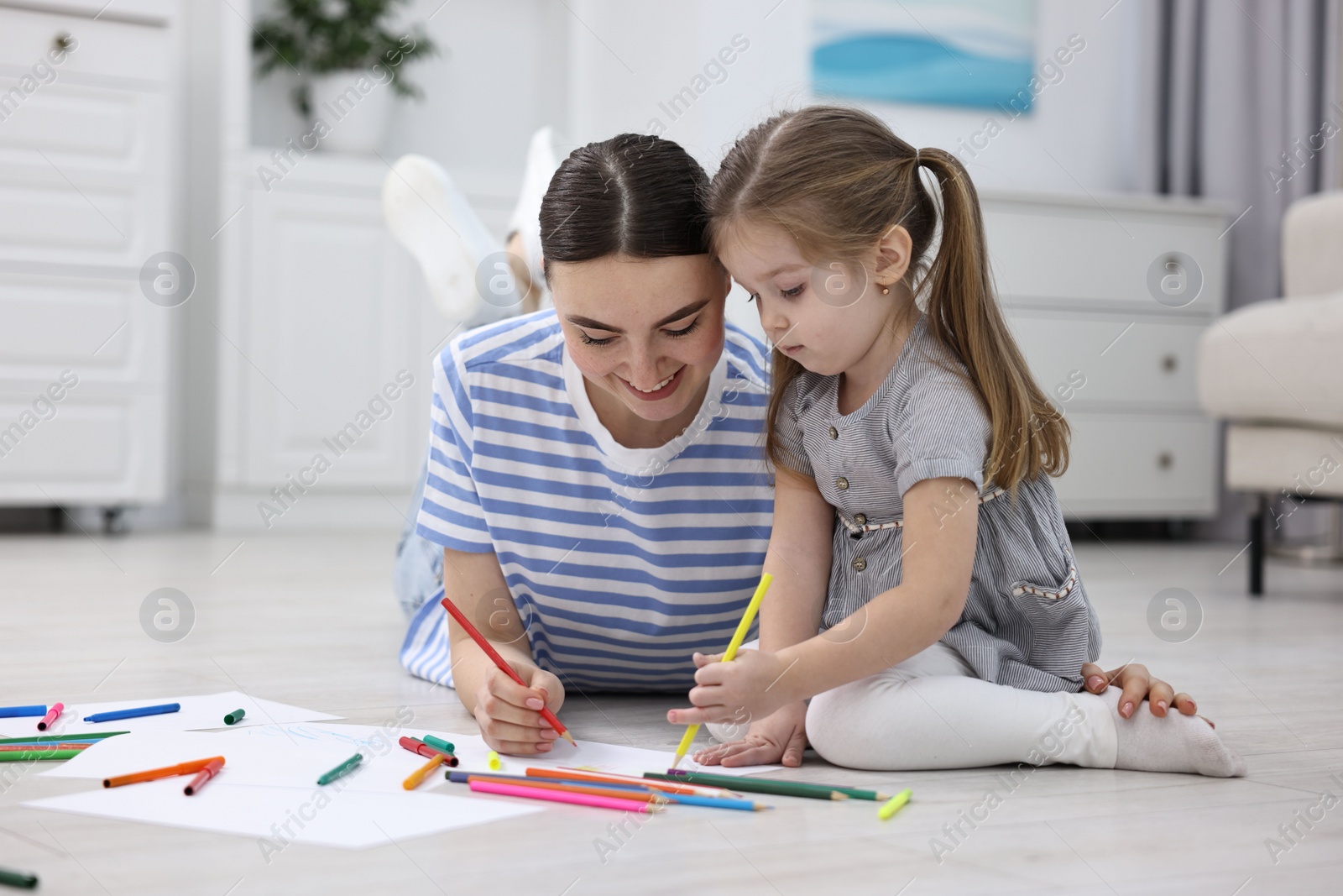 Photo of Mother and her little daughter drawing with colorful markers on floor at home