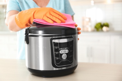 Photo of Woman cleaning modern multi cooker at table in kitchen, closeup