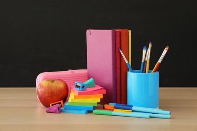 Photo of Different school stationery and apple on wooden table near blackboard. Back to school