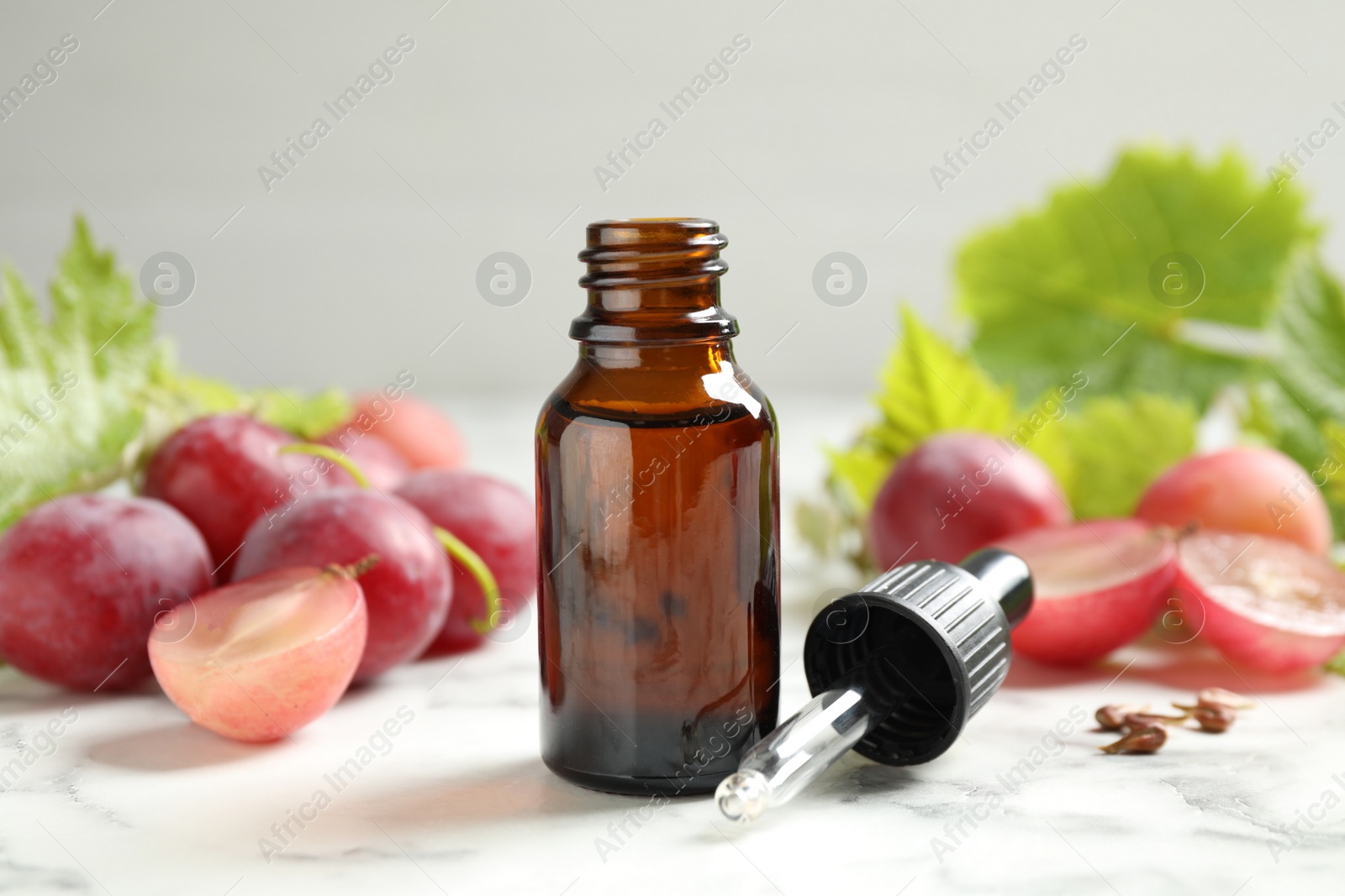 Photo of Bottle of natural grape seed oil on white marble table. Organic cosmetic