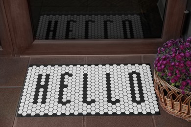 Photo of Stylish door mat with word HELLO and beautiful flowers near entrance