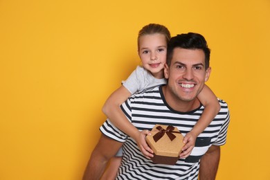 Photo of Man receiving Father's Day gift from his daughter on yellow background. Space for text