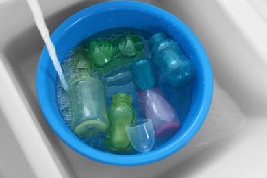 Photo of Light blue basin with baby bottles under stream of water in sink, top view