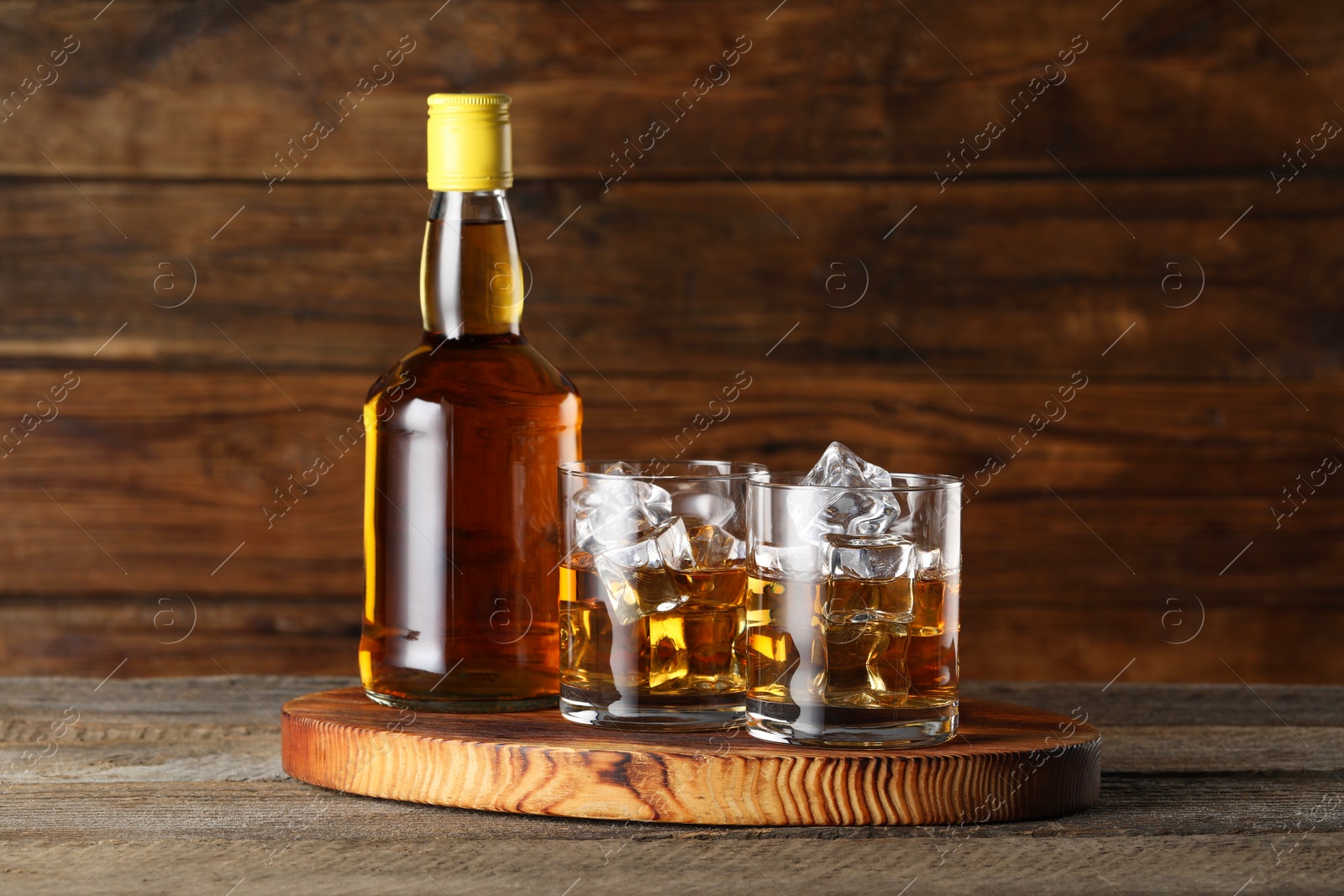 Photo of Whiskey with ice cubes in glasses and bottle on wooden table