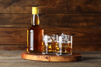 Whiskey with ice cubes in glasses and bottle on wooden table