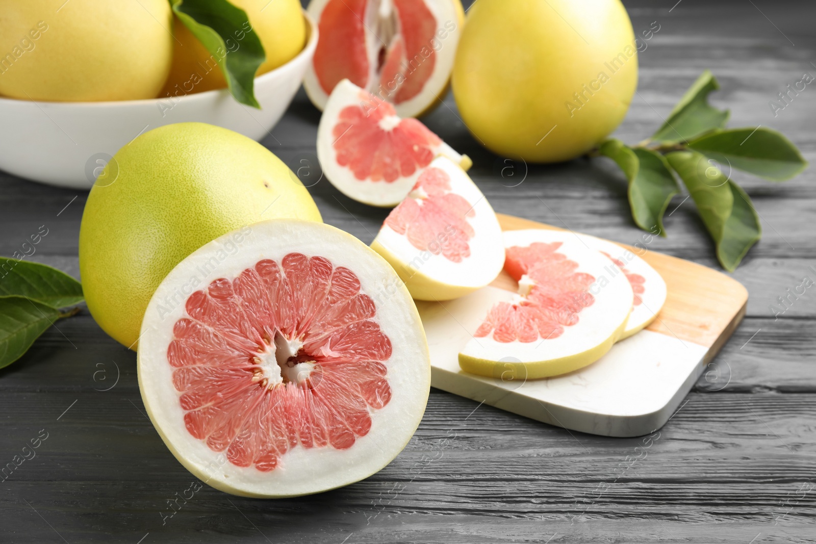 Photo of Fresh cut and whole pomelo fruits on grey wooden table, closeup