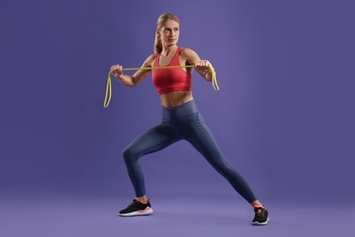 Photo of Athletic woman exercising with elastic resistance band on purple background