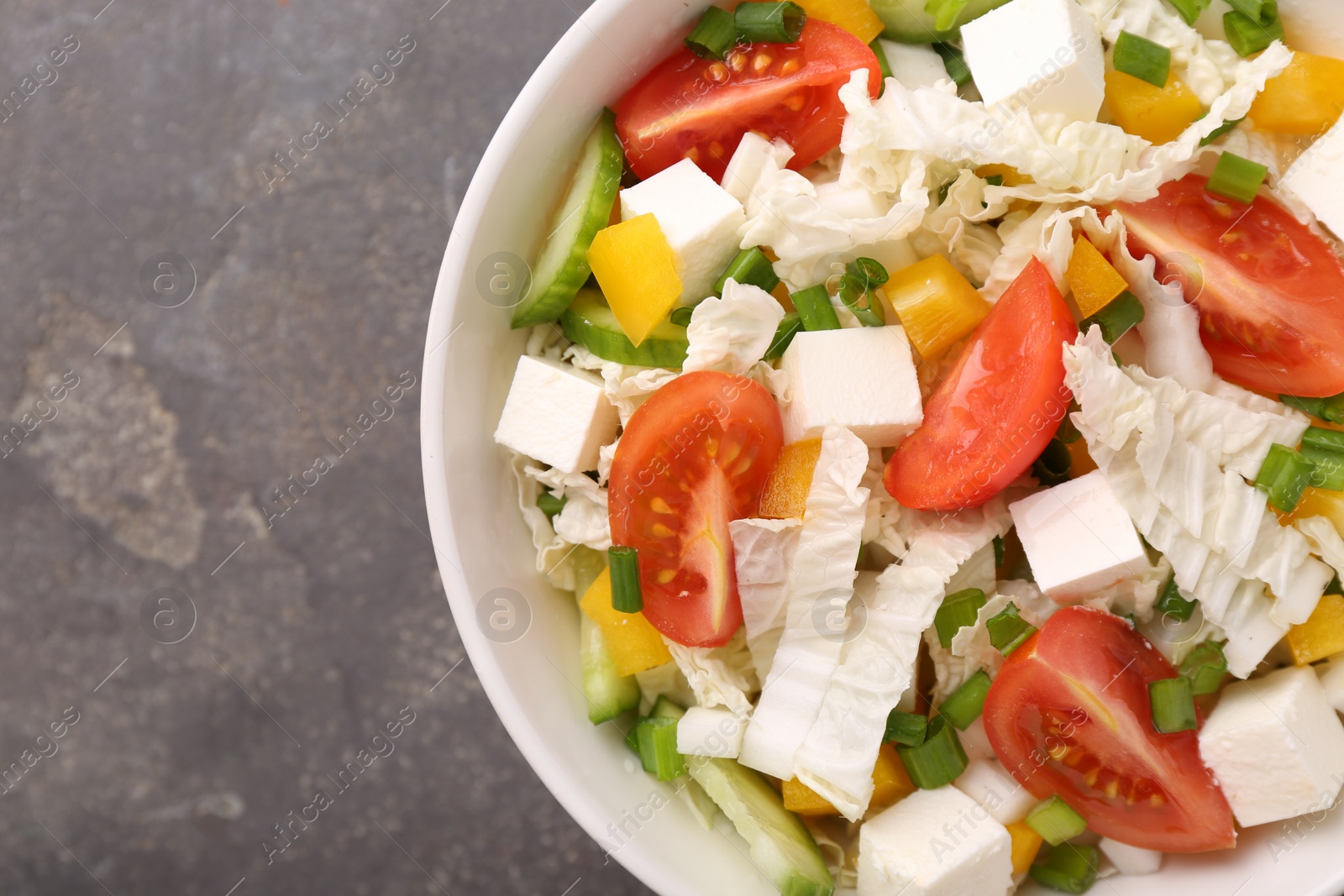 Photo of Tasty salad with Chinese cabbage, tomato, cheese, pepper and cucumber on grey table, top view