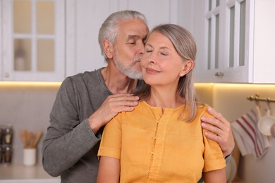 Photo of Senior man kissing his beloved woman in kitchen