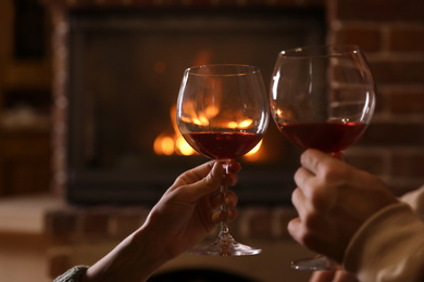 Lovely couple with glasses of wine near fireplace indoors, closeup. Winter vacation