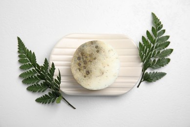 Photo of Soap bar with dish and green leaves on white background, top view. Eco friendly personal care product