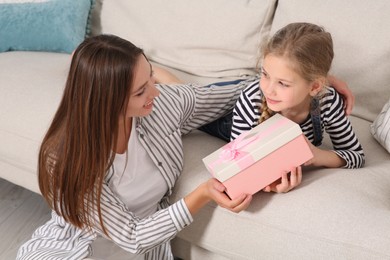 Cute little girl presenting her mother with gift on sofa at home