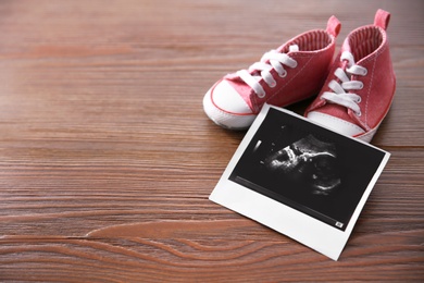 Ultrasound picture and baby shoes on wooden background. Space for text